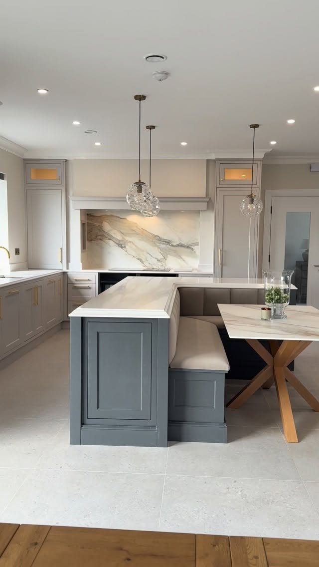 Grey kitchen half island with white marble top and integrated dining nook seating.