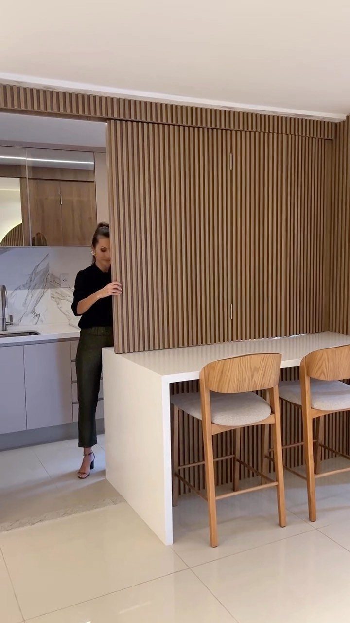 White kitchen half island with wooden bar stools and a slatted wood wall partition.