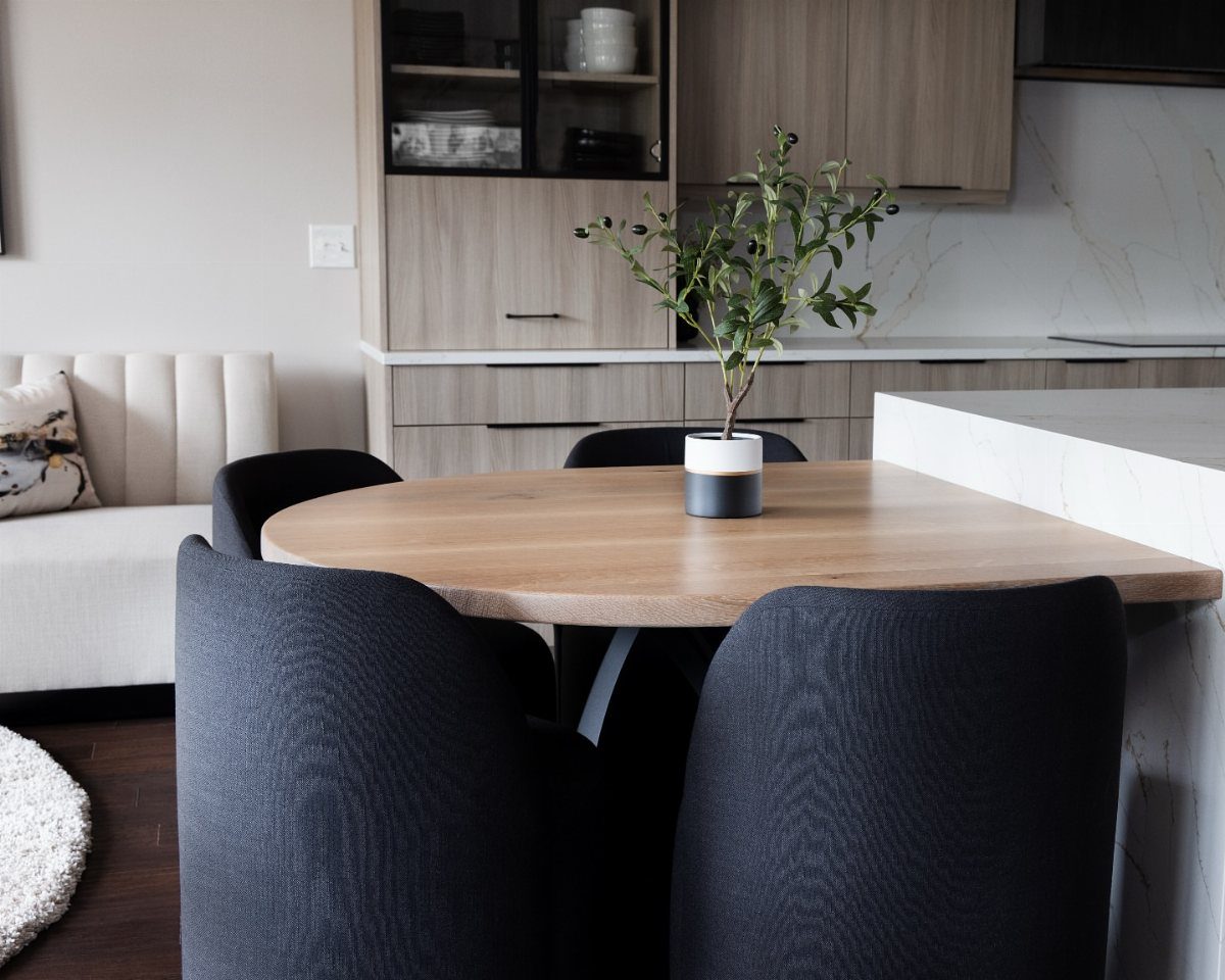 White marble kitchen island with an attached light-wood dining table and black chairs.