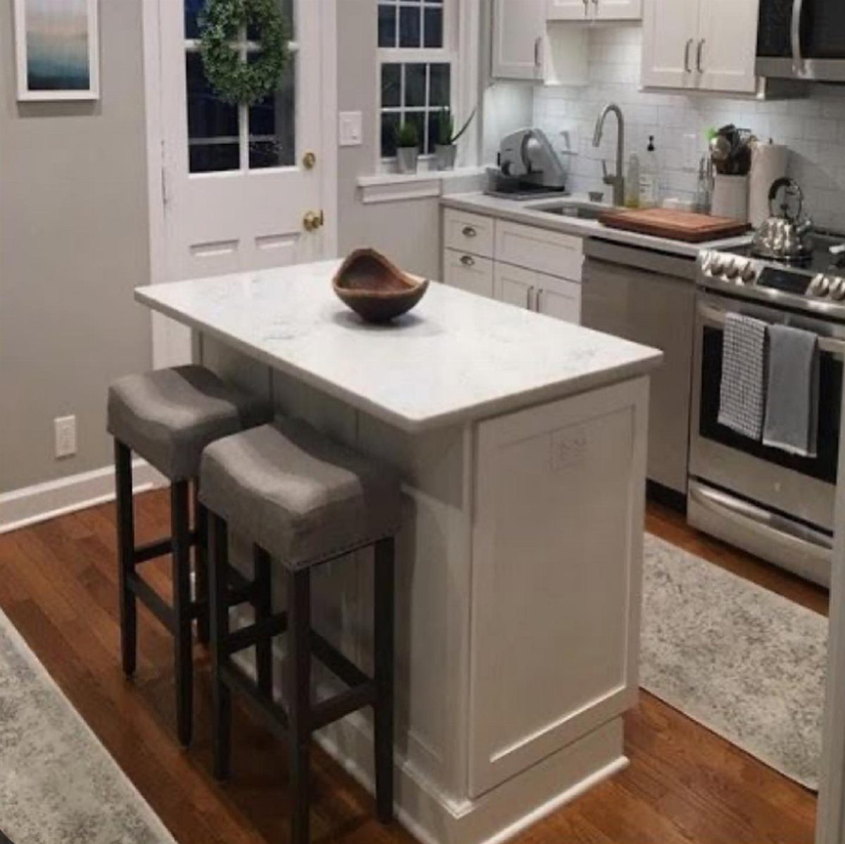 Small white kitchen island with marble top and two grey bar stools.