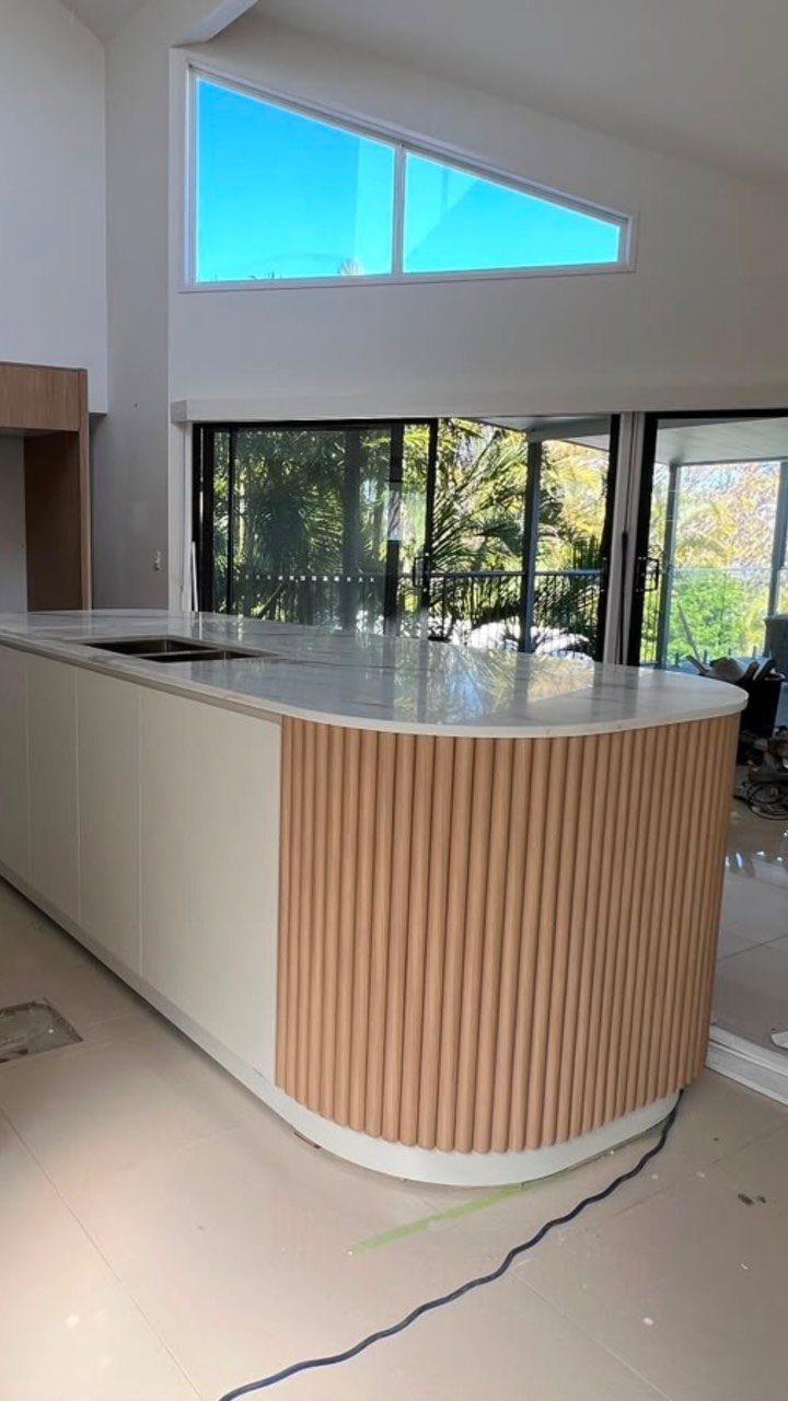 White kitchen island with a curved end and vertical light-brown wooden slat detailing.