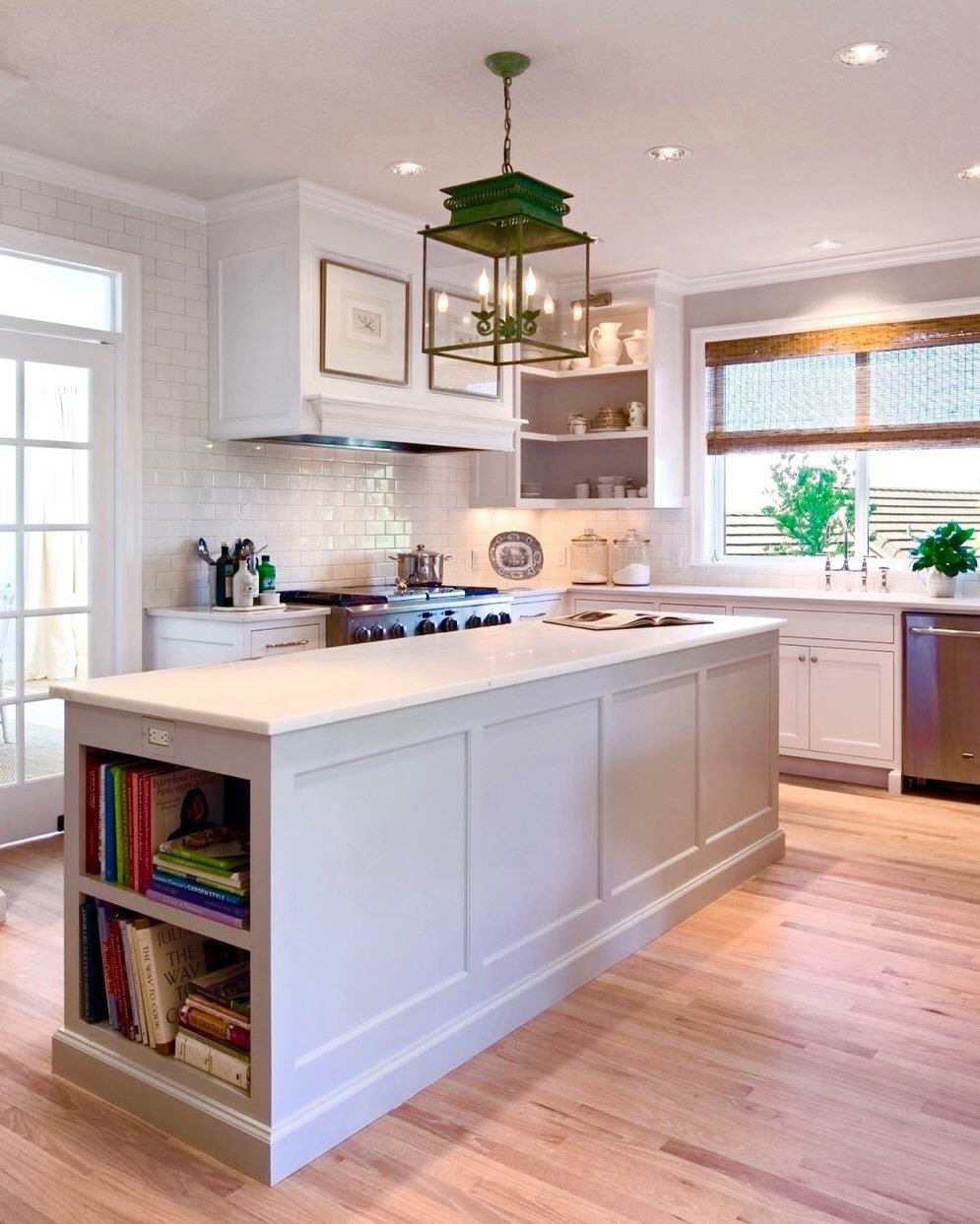 Narrow white kitchen island with built-in bookshelves and a white countertop in a bright kitchen.