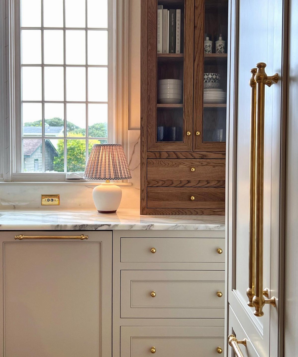 White Cabinets: 13 Kitchen Remodel Ideas 5 White kitchen cabinets featuring brass hardware and a white marble countertop near a window.