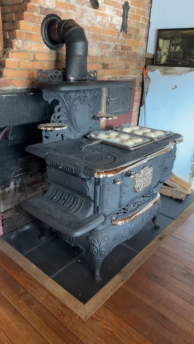 17 Kitchen Stoves Ideas for Every Style and Cooking Need 16 Antique black cast-iron wood-burning stove with baking rolls on top against brick wall.