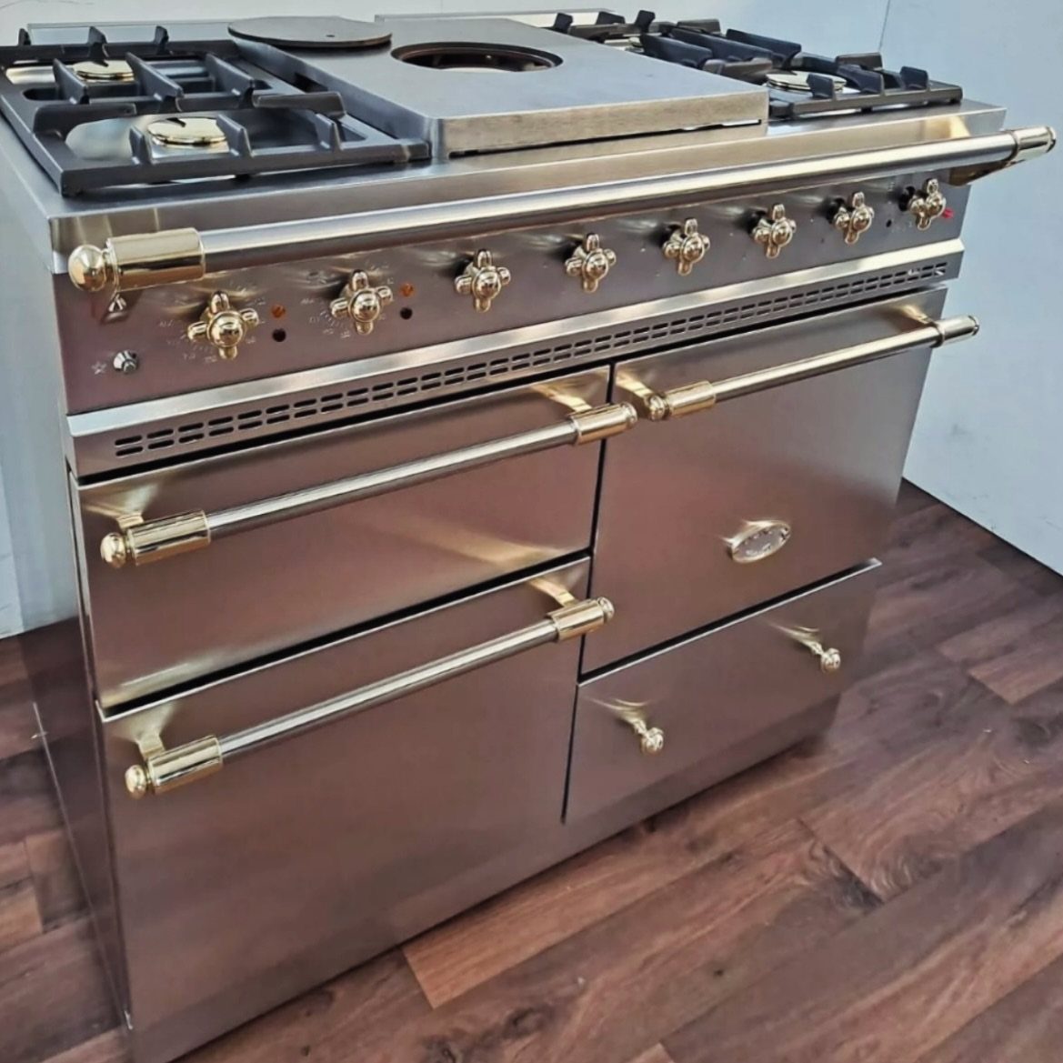 17 Kitchen Stoves Ideas for Every Style and Cooking Need 5 Large stainless steel professional gas range with gold accents on dark wood flooring.
