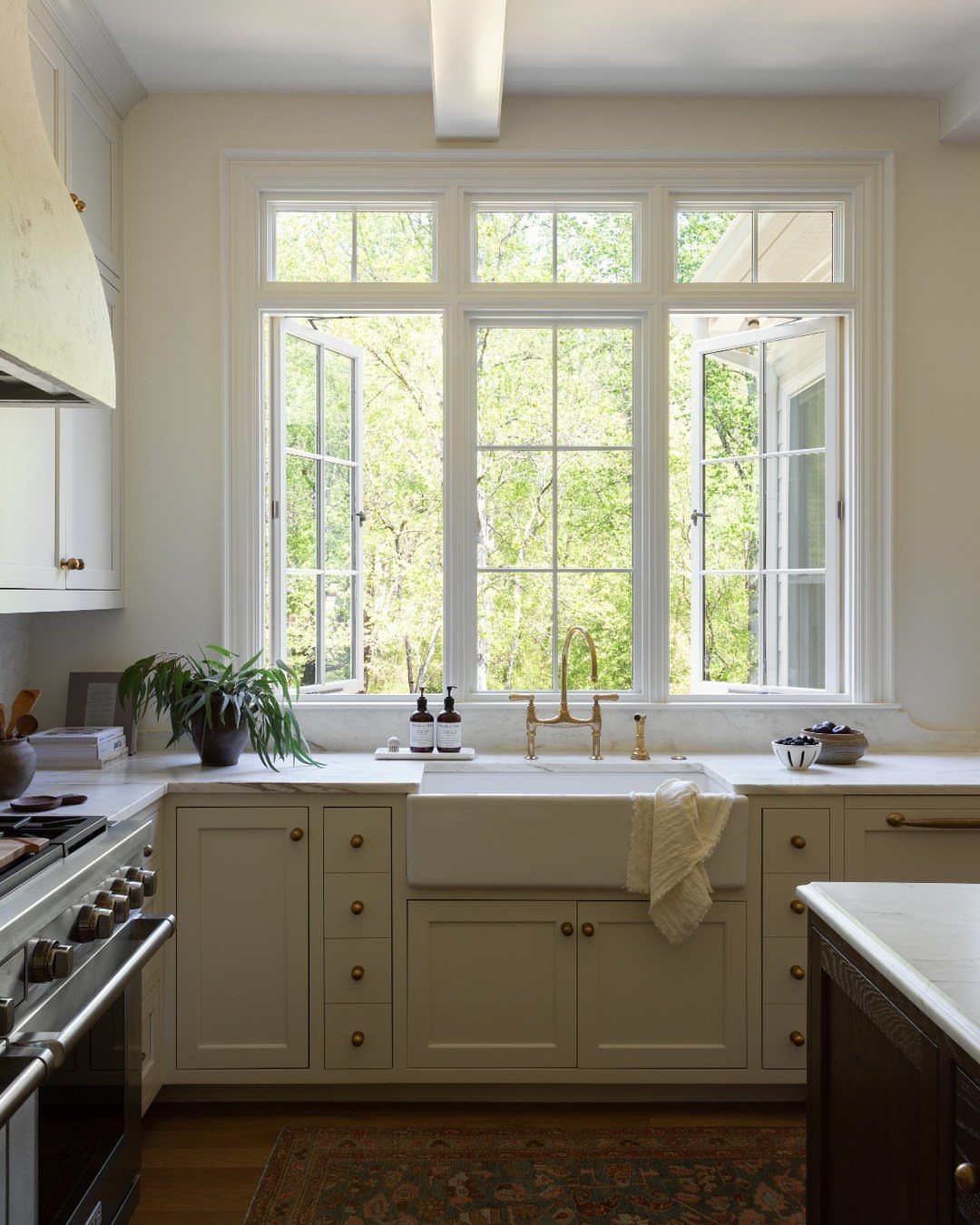 White casement windows open above a farmhouse sink in a bright, airy kitchen.