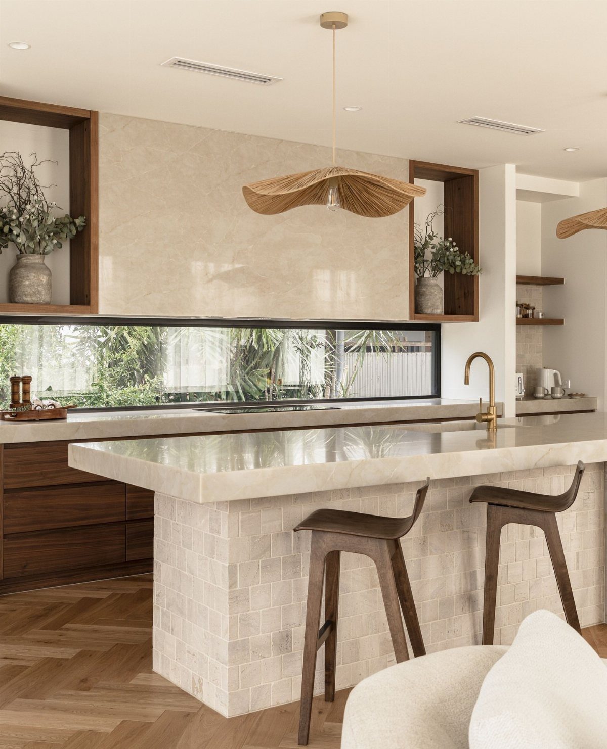 Long horizontal kitchen window overlooking greenery with a stone island and wooden stools.