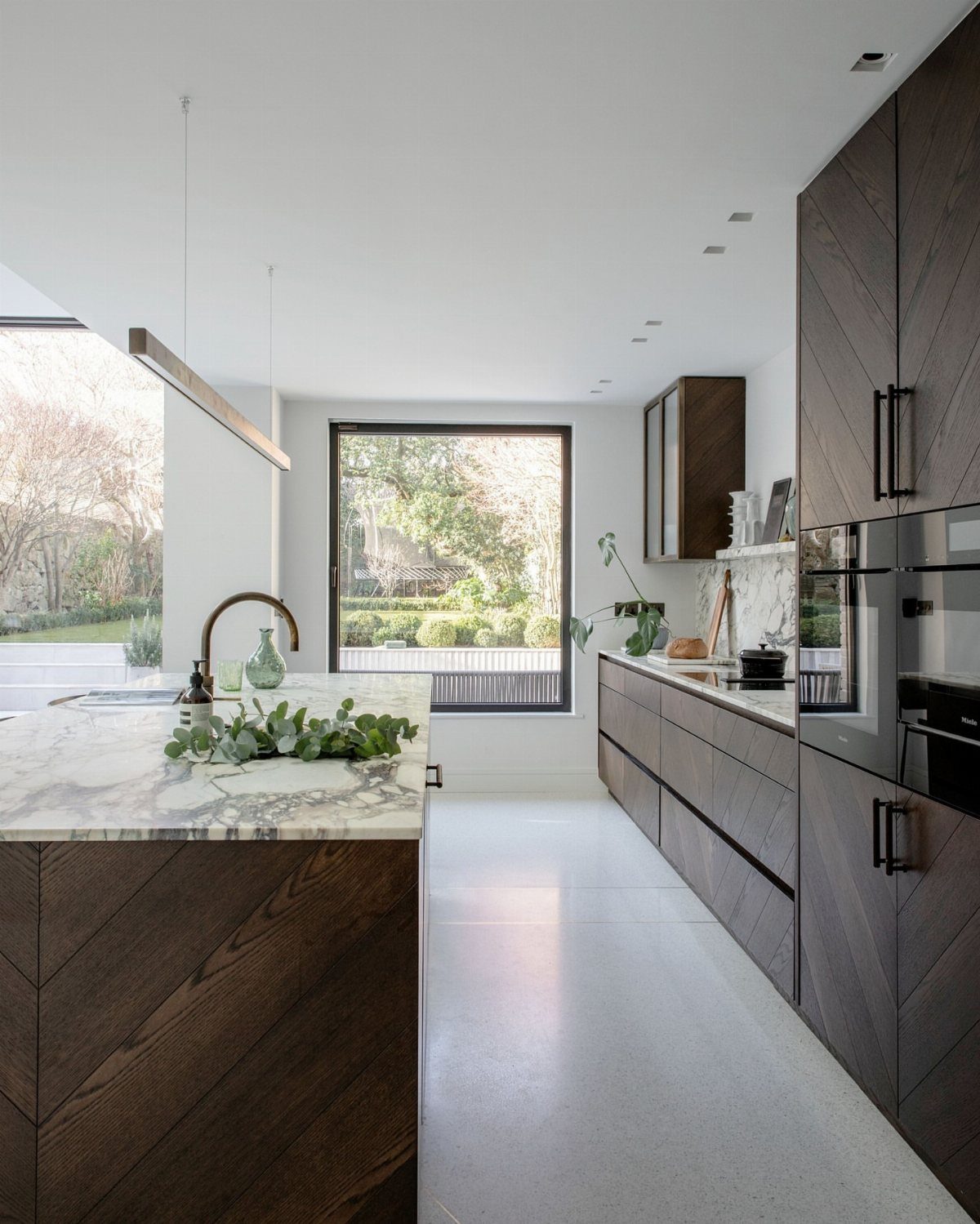 Large black-framed picture window in a modern kitchen overlooking a lush green garden.