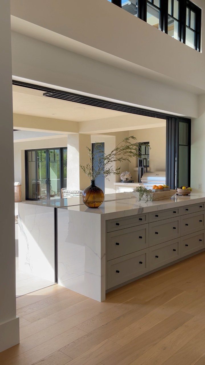 Black-framed pocket sliding window open in a modern kitchen with white marble island.
