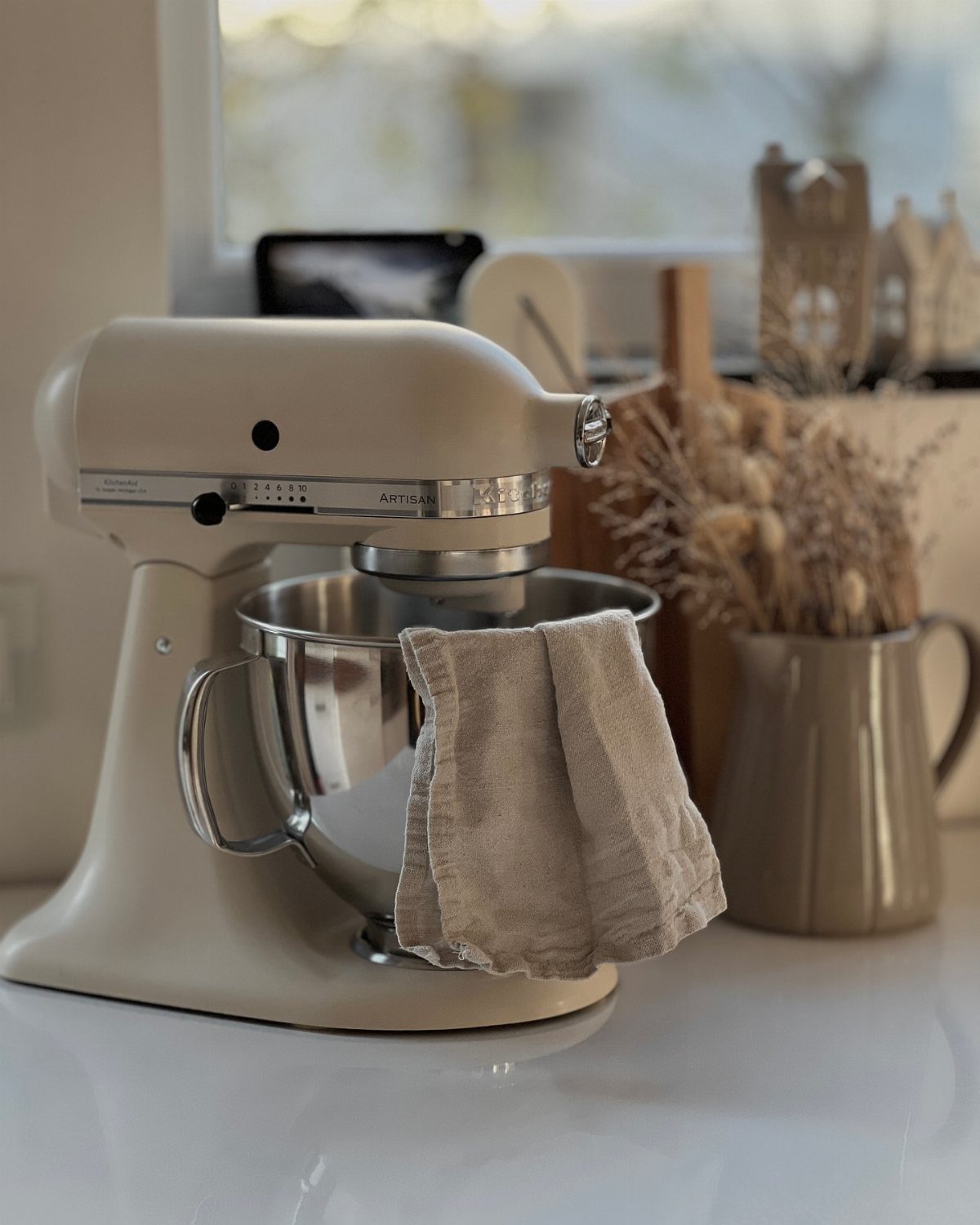 Matte beige KitchenAid stand mixer with stainless steel bowl and linen cloth.