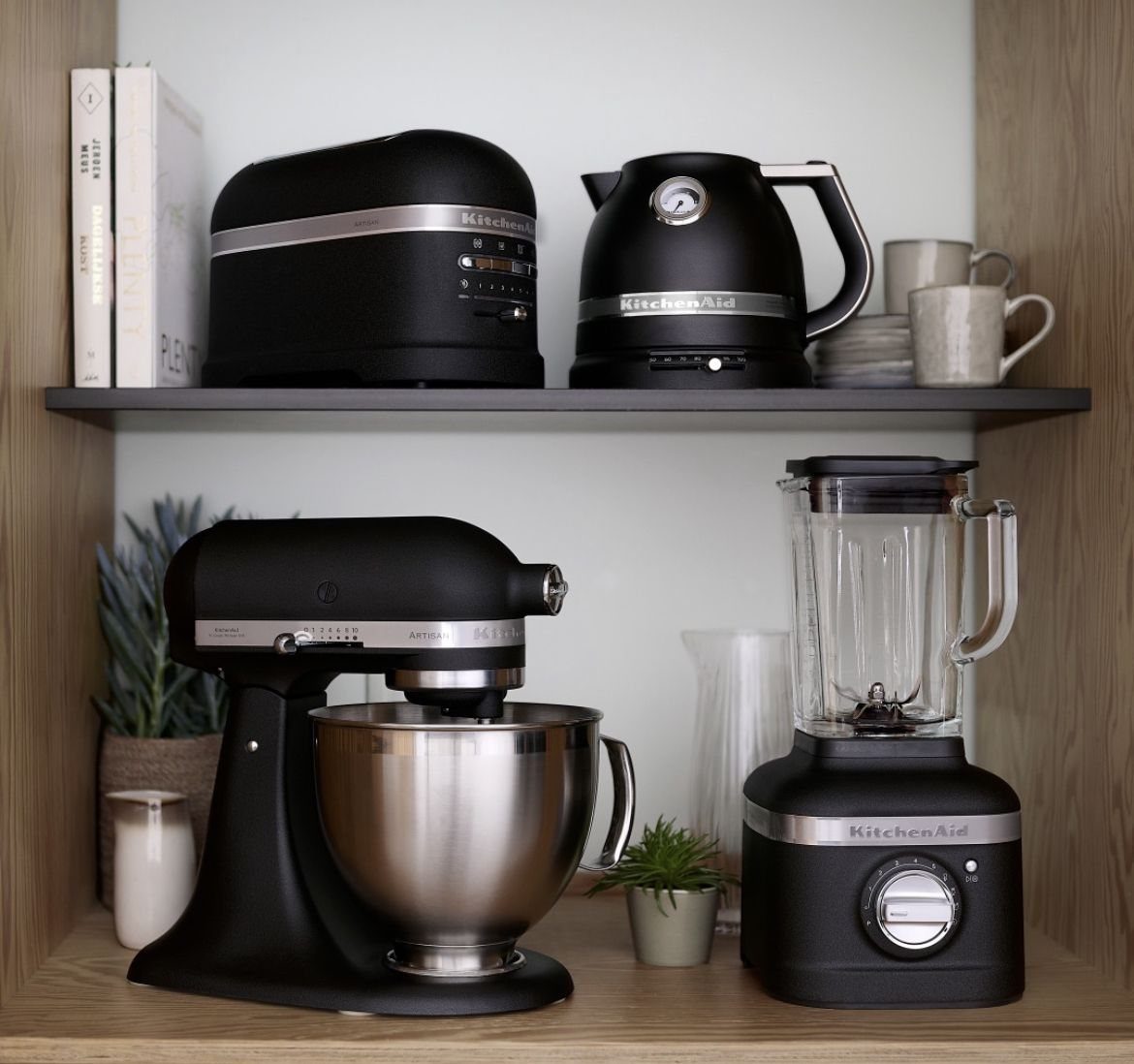 Matte black KitchenAid mixer and kettle on light wood kitchen shelving.