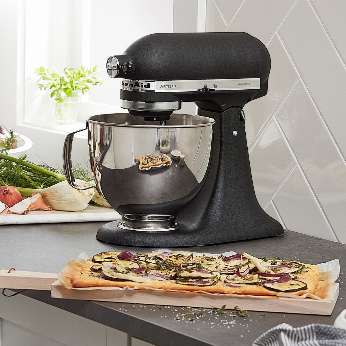 Matte black KitchenAid stand mixer with stainless steel bowl and flatbread on countertop