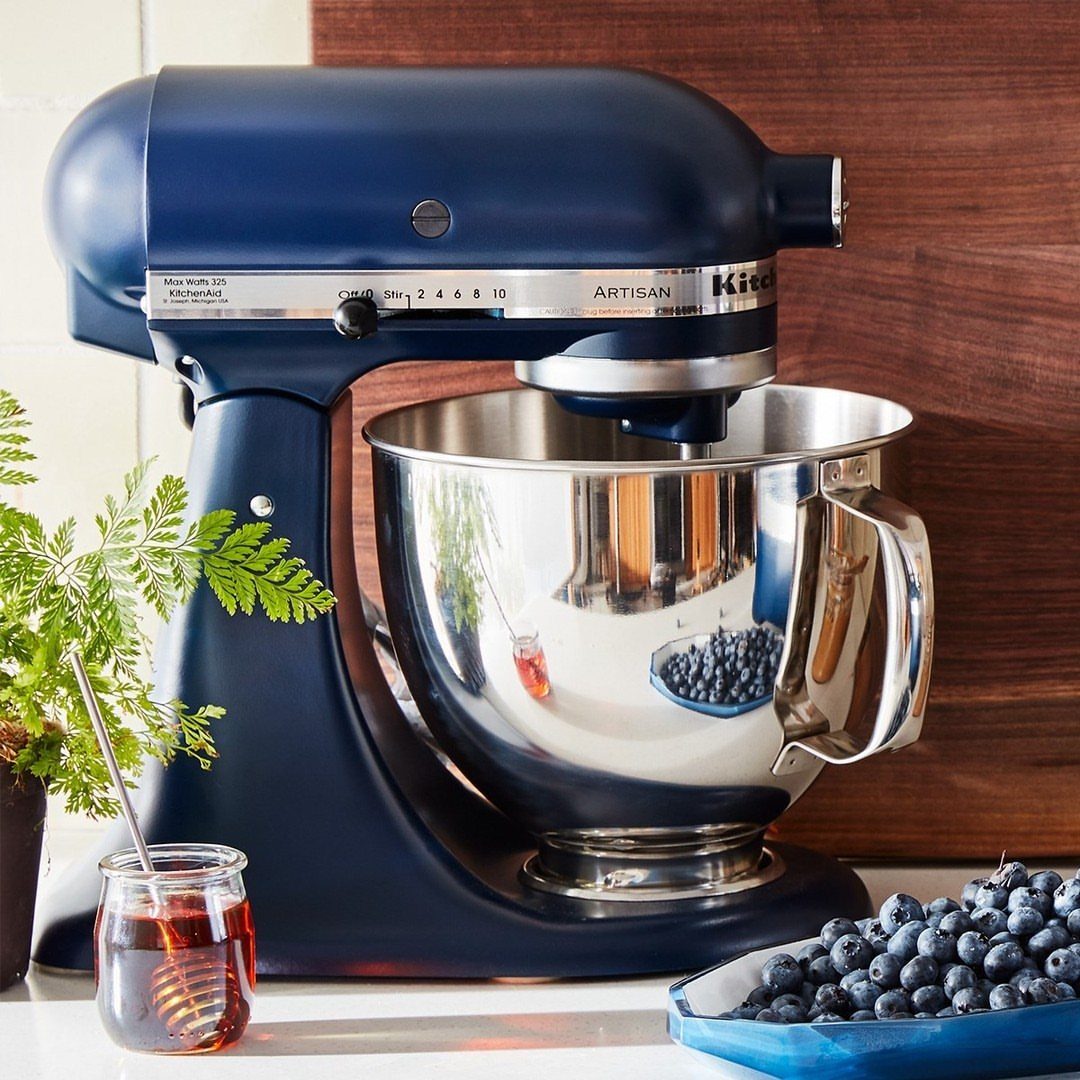 Dark blue KitchenAid Artisan stand mixer with stainless steel bowl and fresh blueberries.