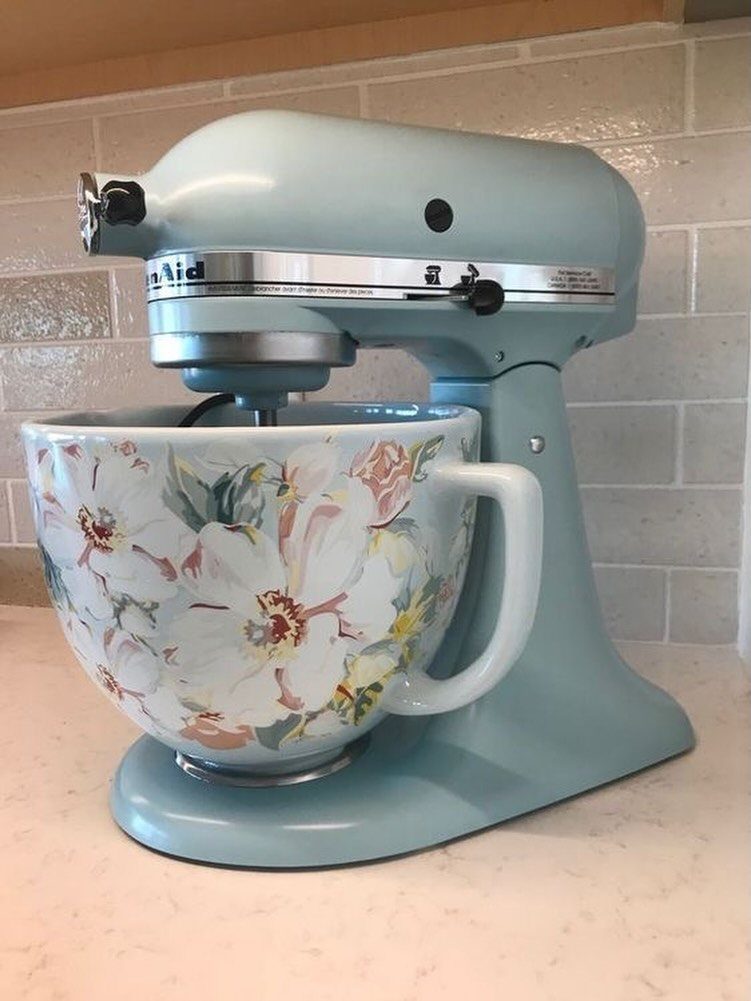 Light blue matte stand mixer with a floral ceramic mixing bowl on a counter.
