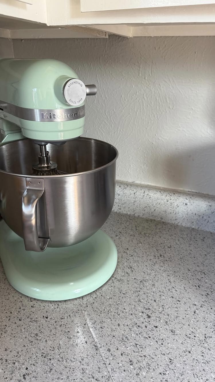 Light green KitchenAid stand mixer with stainless steel bowl on speckled countertop.