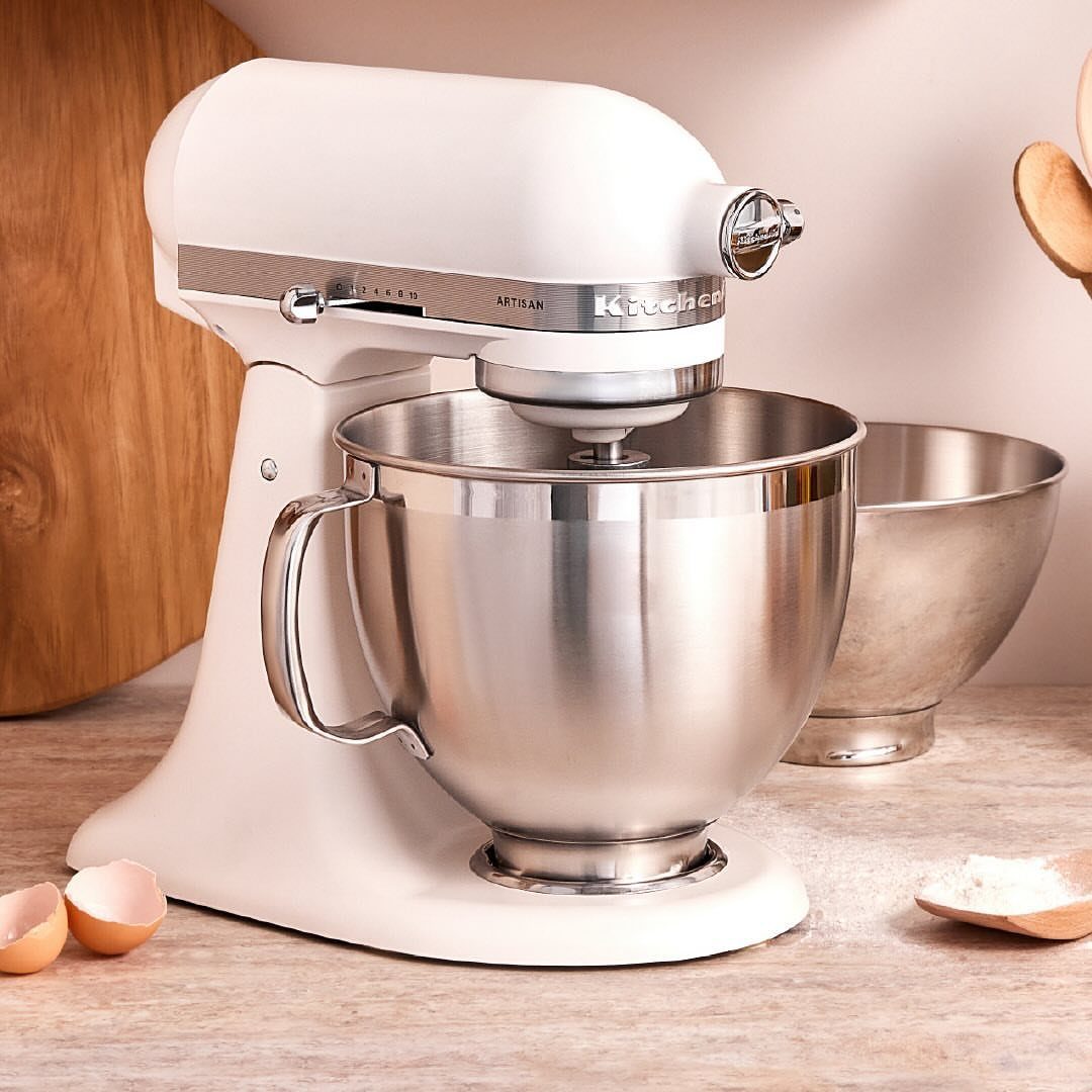 Off-white matte KitchenAid stand mixer with a stainless steel bowl on a countertop.