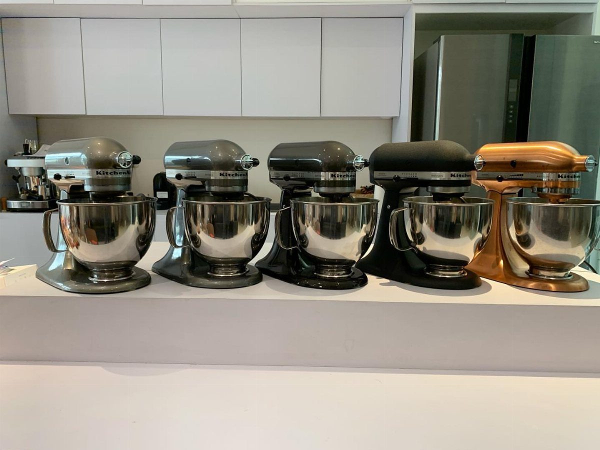 Five KitchenAid stand mixers in different colors lined up on a white countertop.