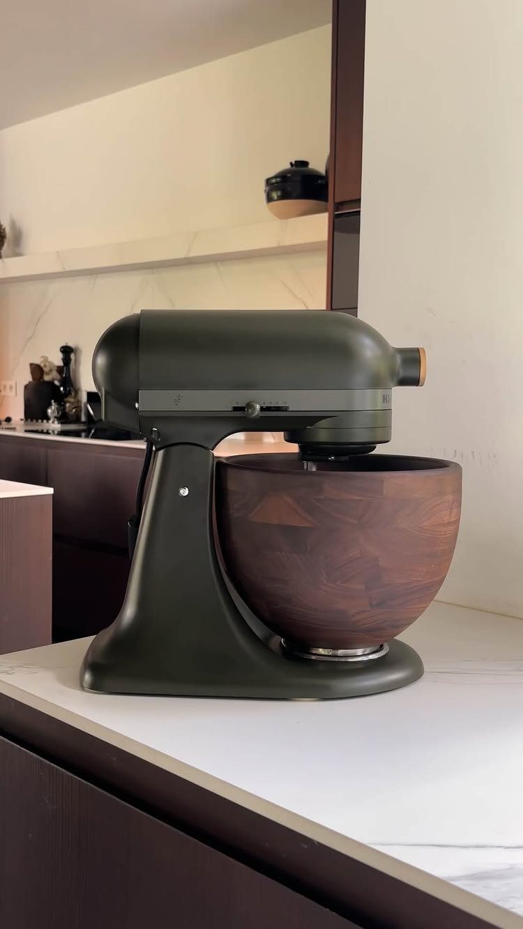 Matte olive green stand mixer with a dark wood bowl on white countertop
