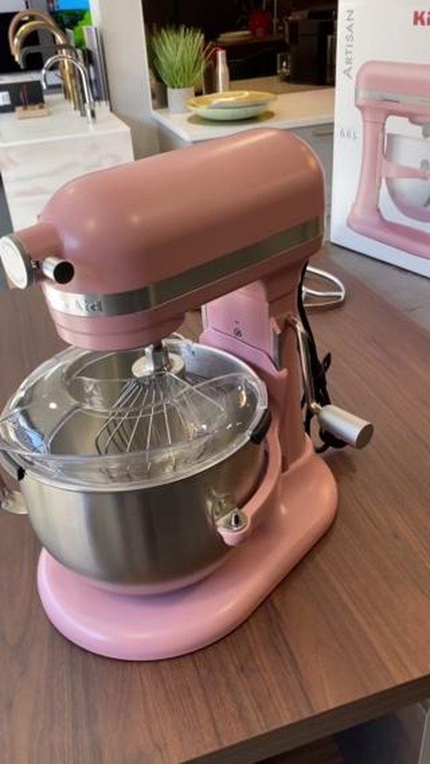 Pink matte KitchenAid stand mixer with stainless steel bowl on a wooden counter.