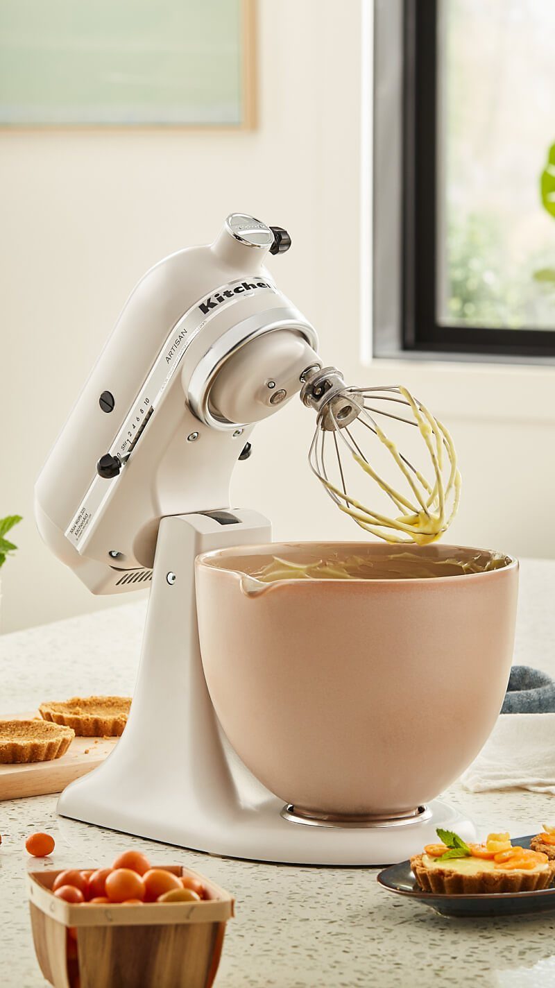 White matte stand mixer with a peach ceramic bowl and whisk on countertop.