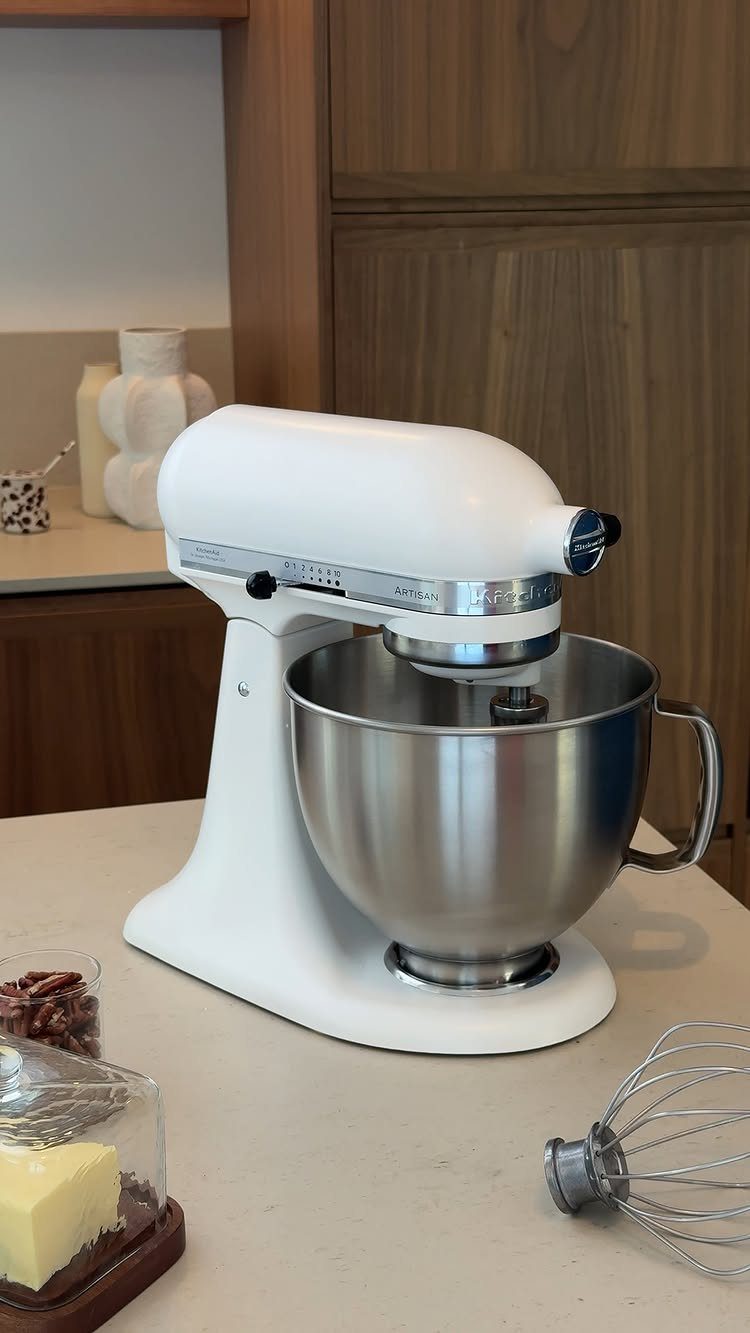 White KitchenAid stand mixer with stainless steel bowl on a light kitchen counter.