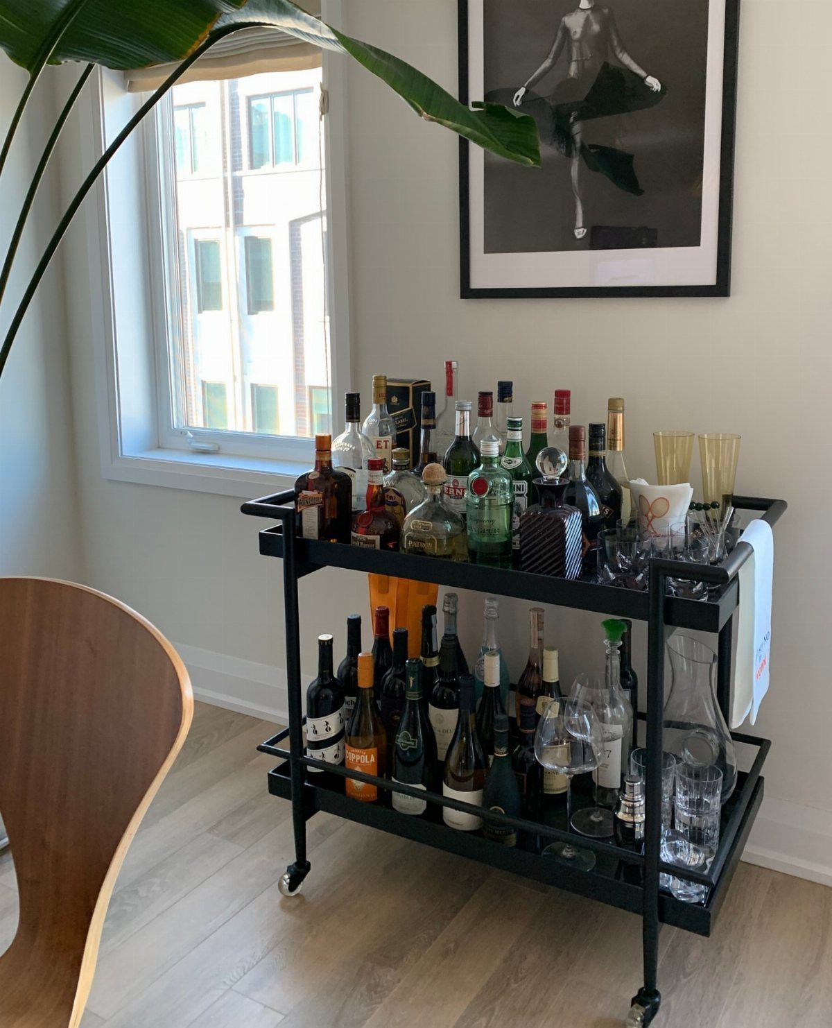 13 Mini Bar House Design Ideas to Fit Your Space and Taste 3 Black metal bar cart on wheels filled with liquor bottles and glassware.