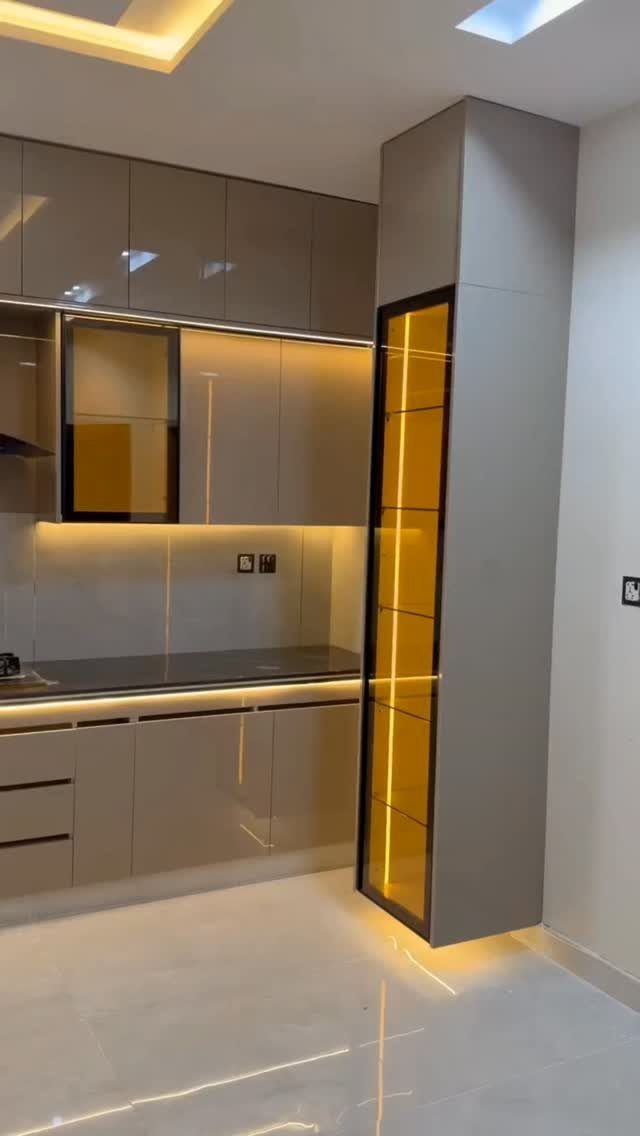 Glossy taupe kitchen cabinets with a smooth handleless design and glowing yellow display cabinet.
