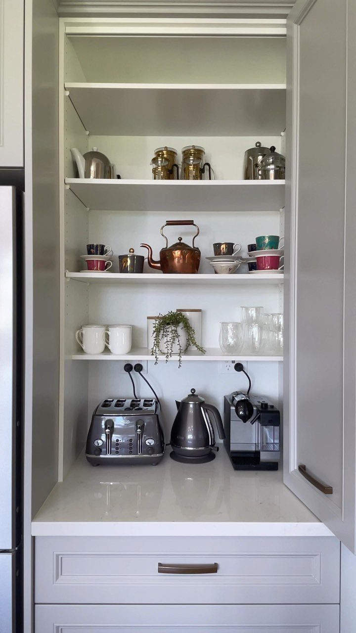White kitchen cabinet with open door concealing a toaster, kettle, and coffee maker.