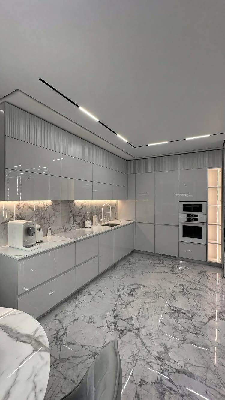 Modern minimalist white kitchen with glossy cabinets and white marble floors and backsplash.