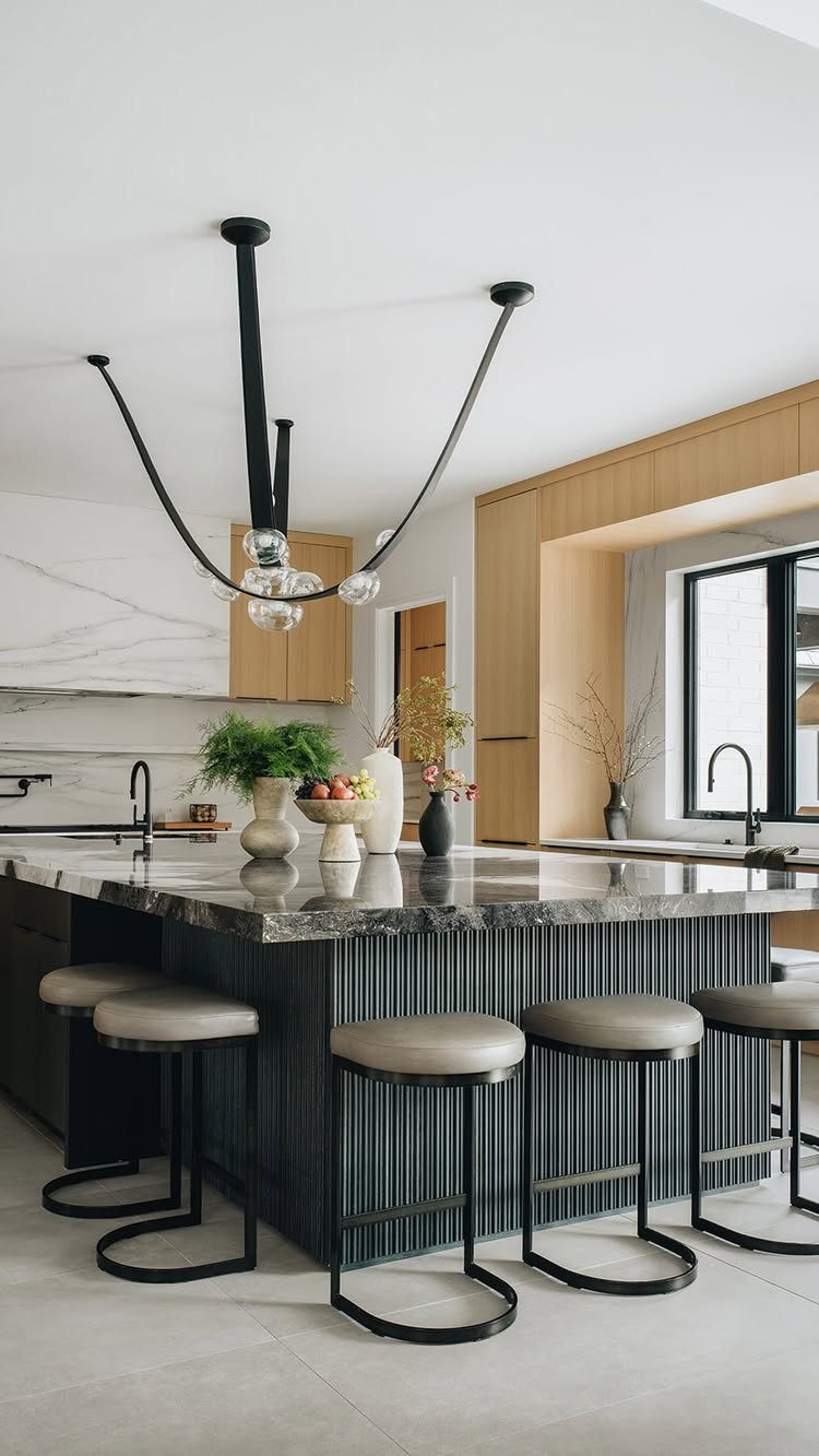 Modern kitchen island with marble top, grey bar stools, and sculptural black lighting.