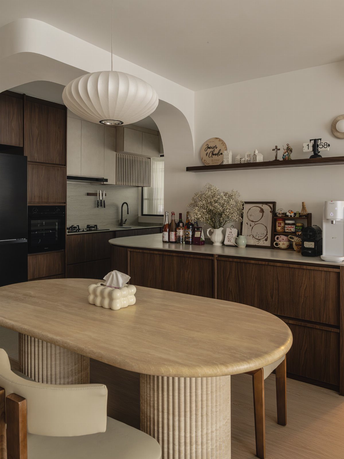 Modern kitchen with dark wood cabinets, light countertops, and a fluted oval wooden table.