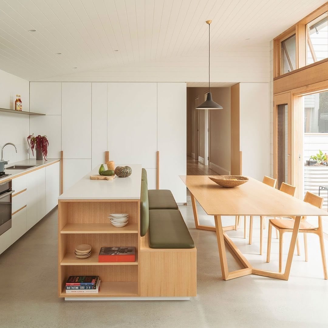 Modern kitchen island with an integrated olive green bench seat and wooden dining table.
