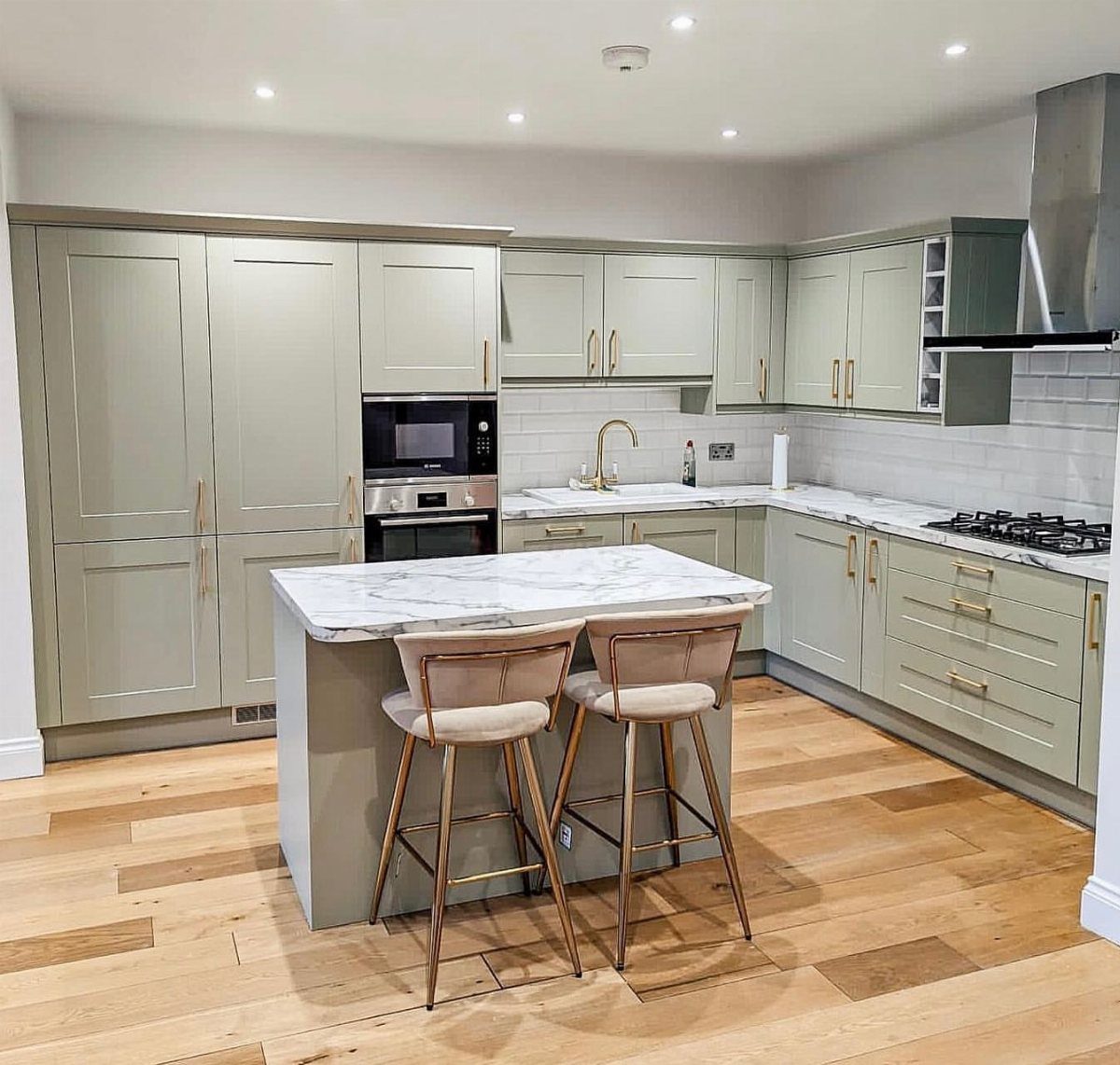 Small sage green kitchen island with white marble top and two beige bar stools