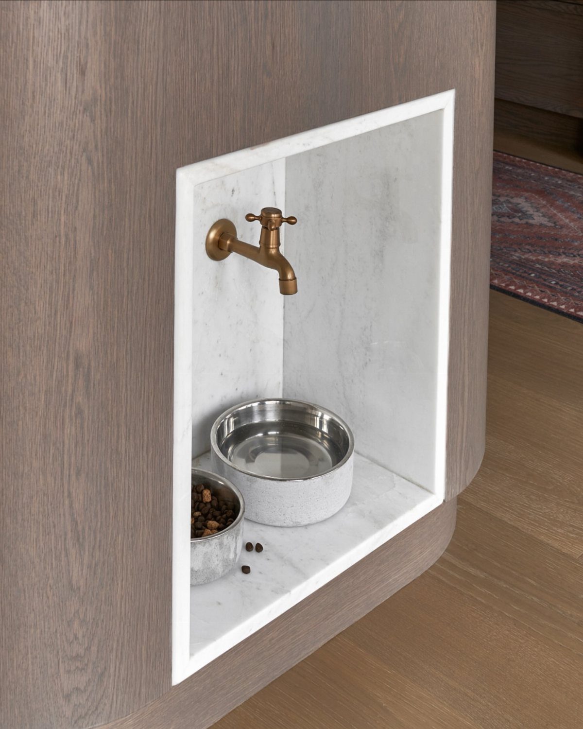 Built-in pet station in a wooden kitchen island with marble niche and brass faucet.