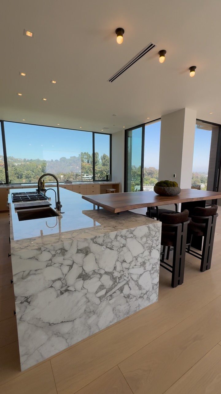 Modern white marble kitchen island with a wooden seating extension and leather bar stools.