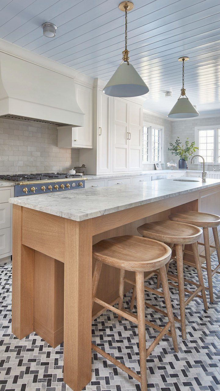 Narrow wooden kitchen island with marble top and three wooden bar stools.