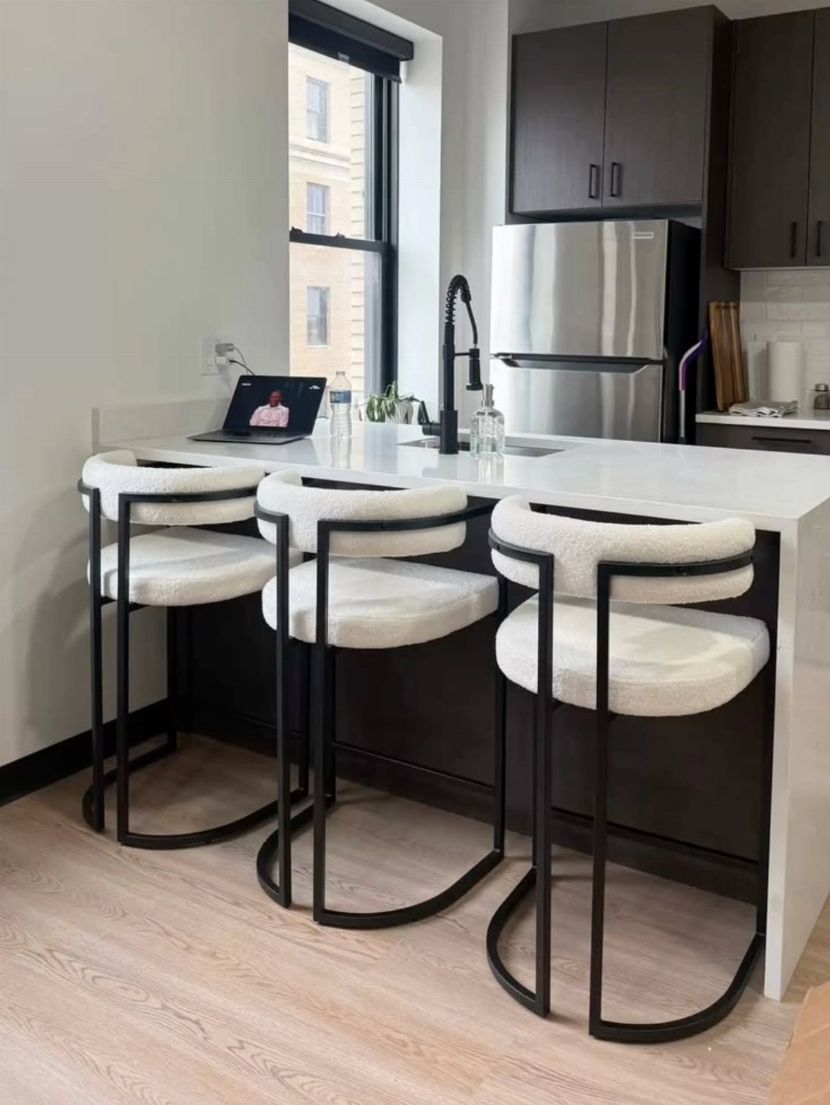 White bouclé counter stools with black frames lined up along a modern kitchen island.