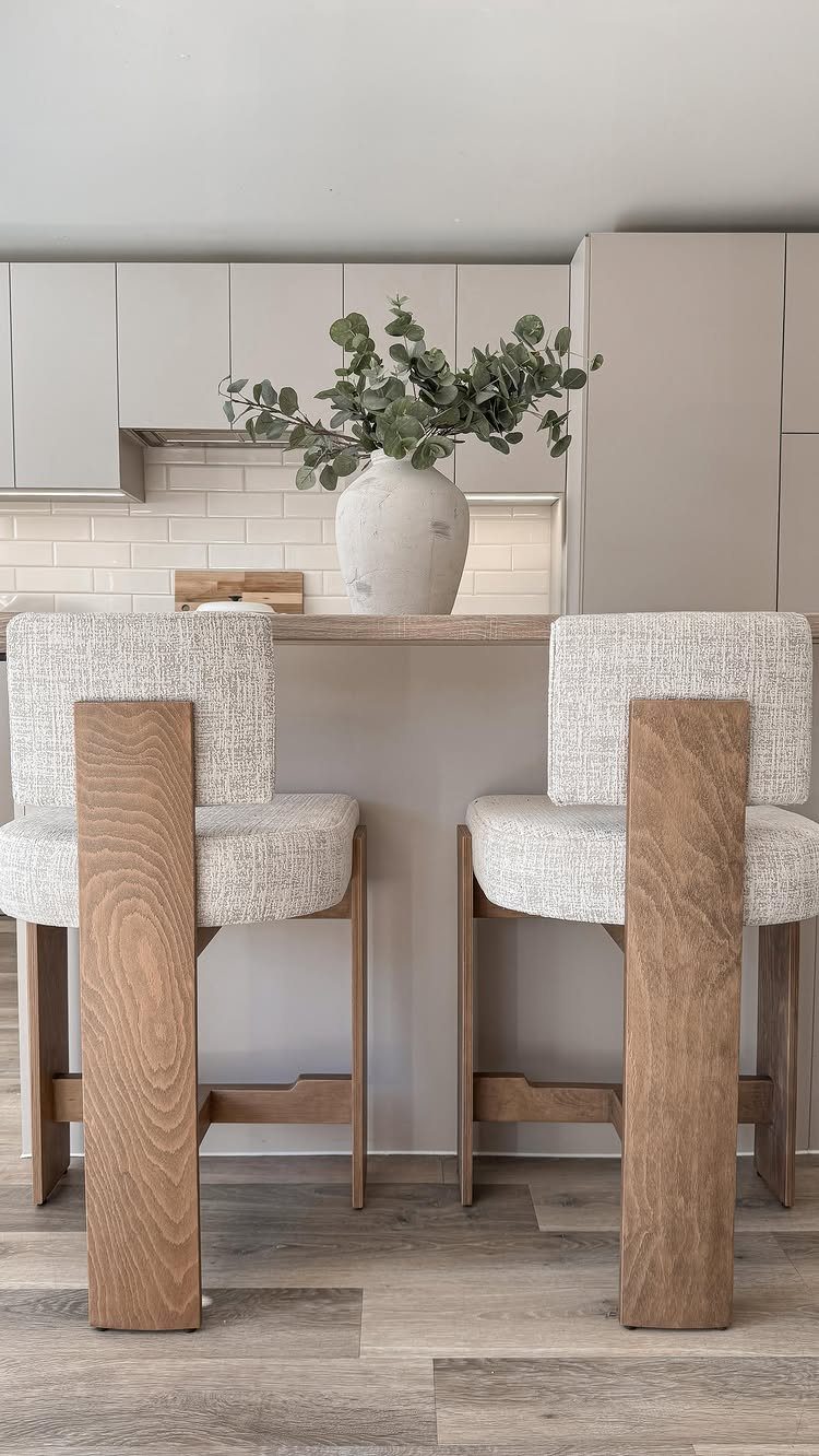 Two white bouclé counter stools with thick light-brown wooden frames at a kitchen island.