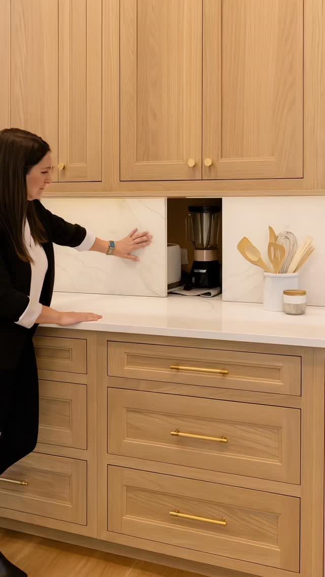 15 Modern Minimalist Home Ideas That Define Clean Living 12 Woman sliding a marble panel to reveal a hidden blender in light wood cabinetry.