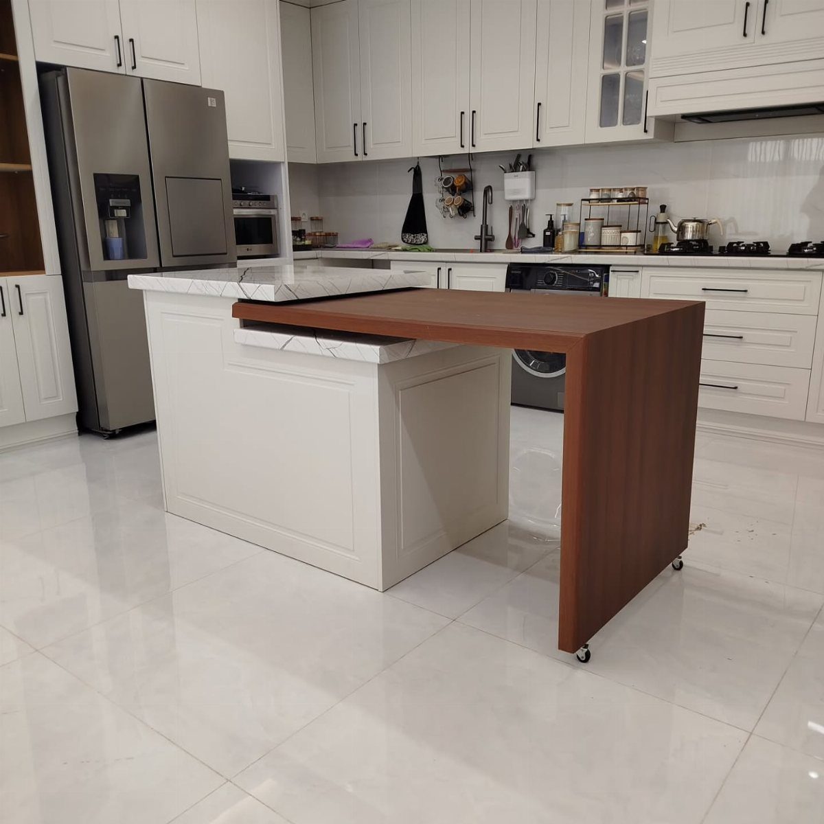 Brown wooden moveable table on wheels next to a white kitchen island.