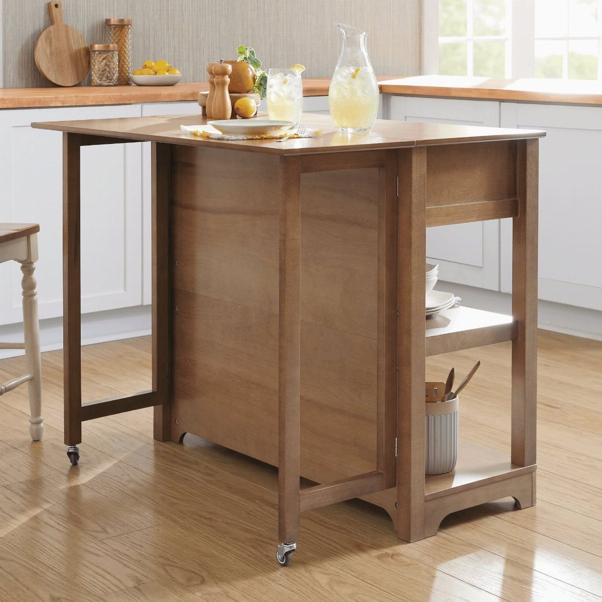 Wooden kitchen island with a raised drop-leaf extension and wheels in a bright kitchen.