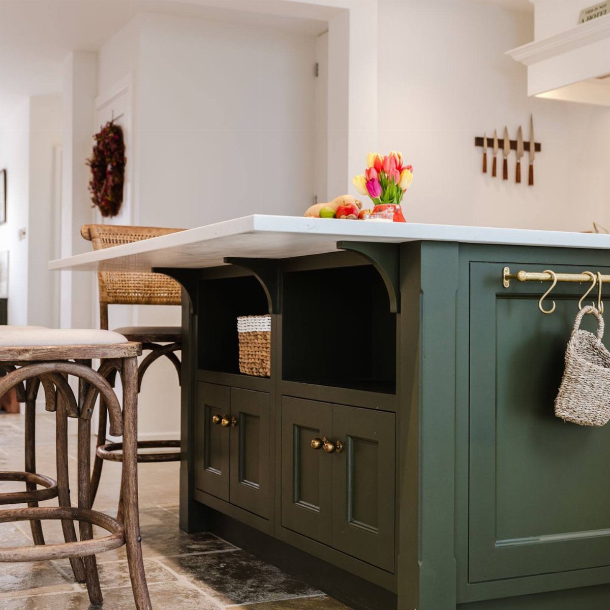 Dark green kitchen island with white countertop overhang and two wooden stools.