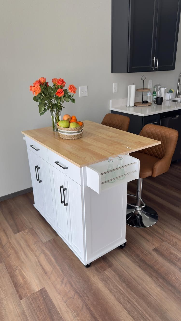 White rolling kitchen island with wood top and two brown leather swivel stools.