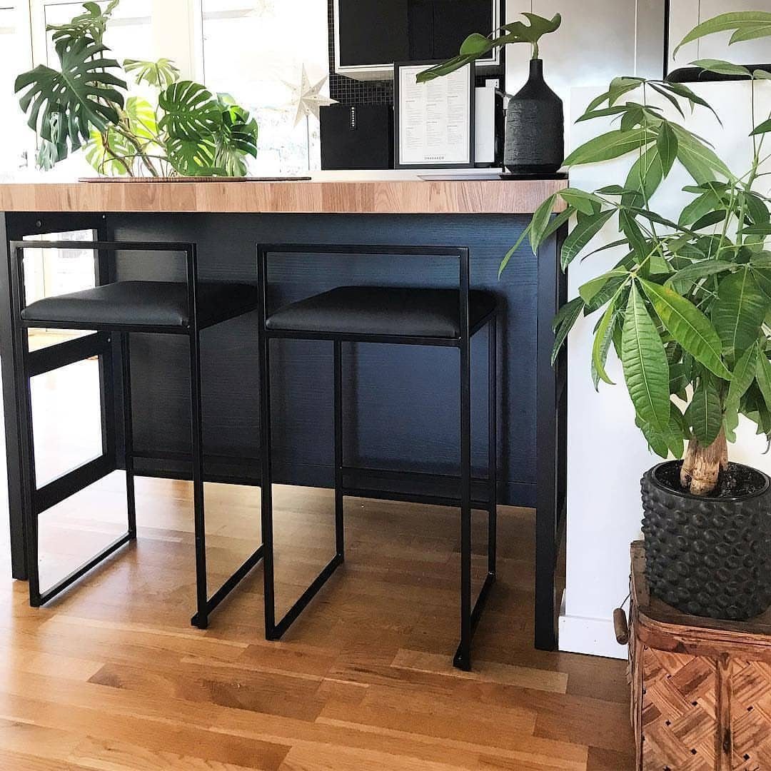 Black kitchen island with wooden top and two black metal bar stools.