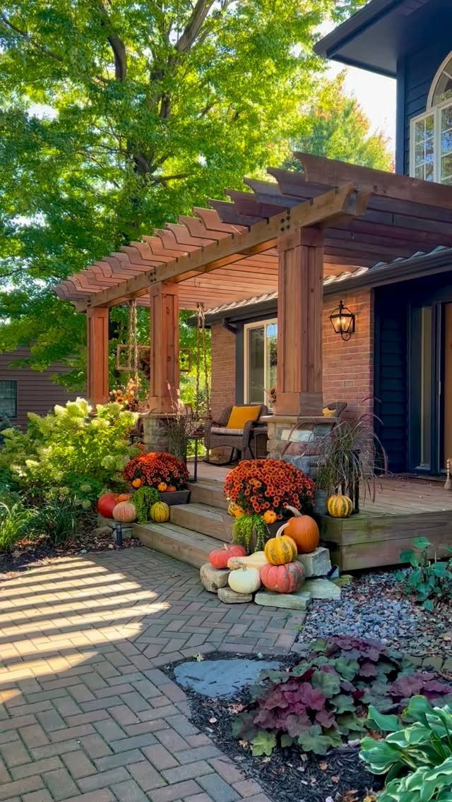 Wooden pergola with a porch swing and autumn decorations on a brick patio.