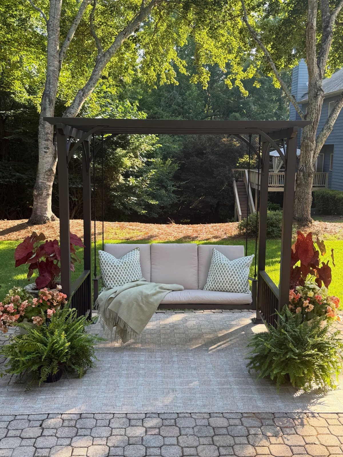 Dark brown wooden pergola with a hanging porch swing on a stone patio