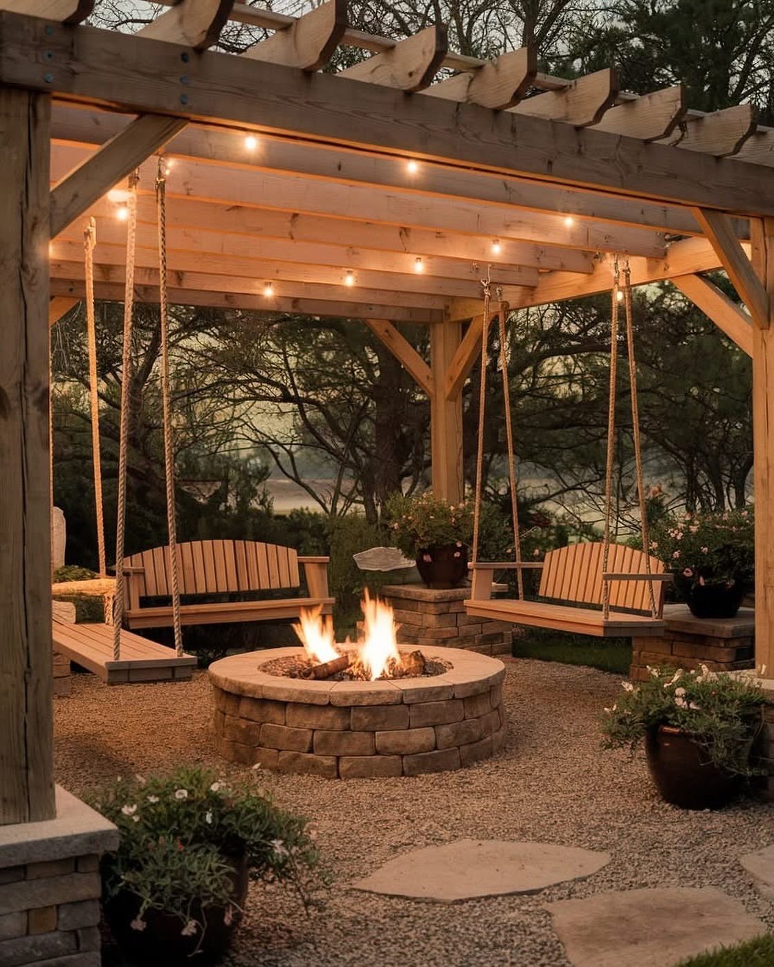 Wooden pergola with two hanging swings and a stone fire pit with flames.