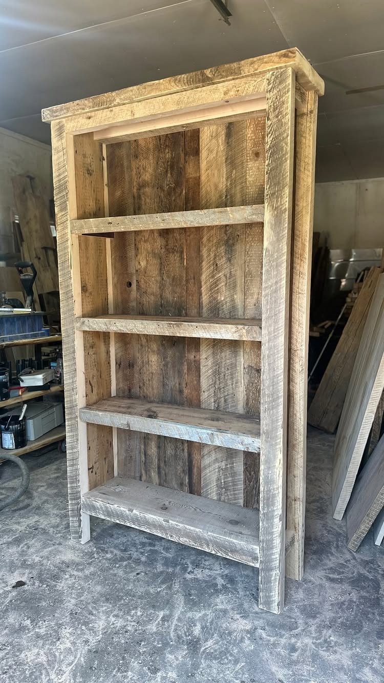Rustic reclaimed wood bookcase with four open shelves in a workshop setting.