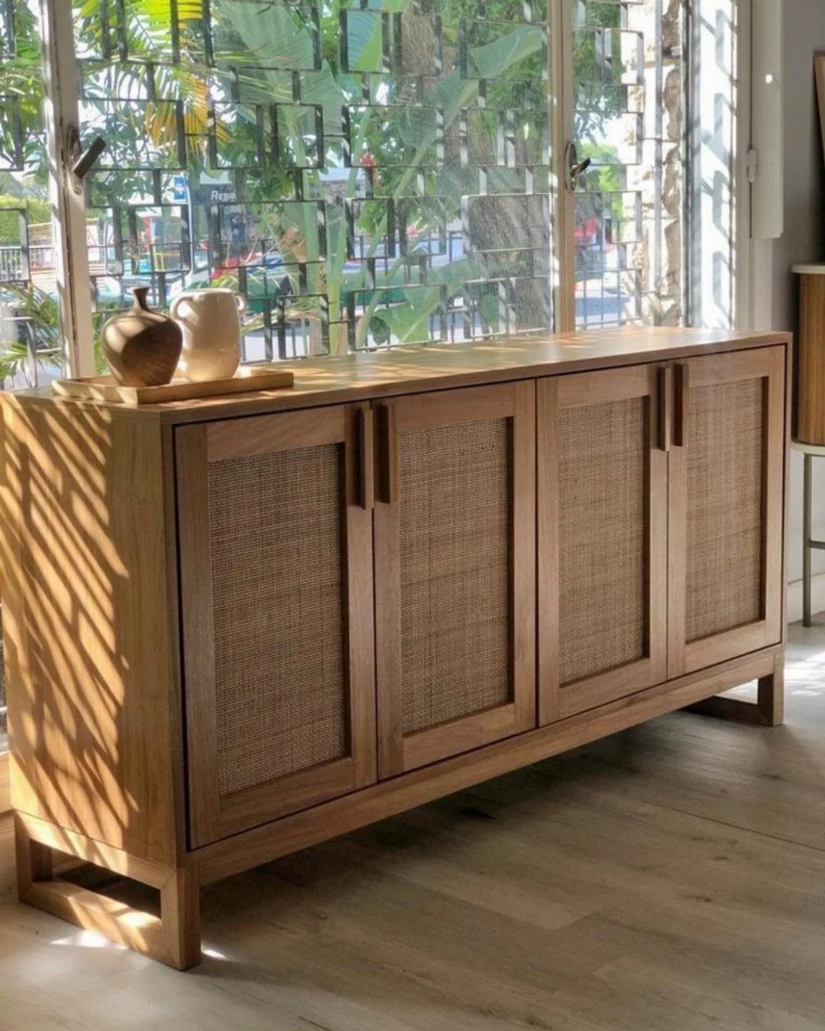 Wooden buffet cabinet with rattan door panels and ceramic vases on top.