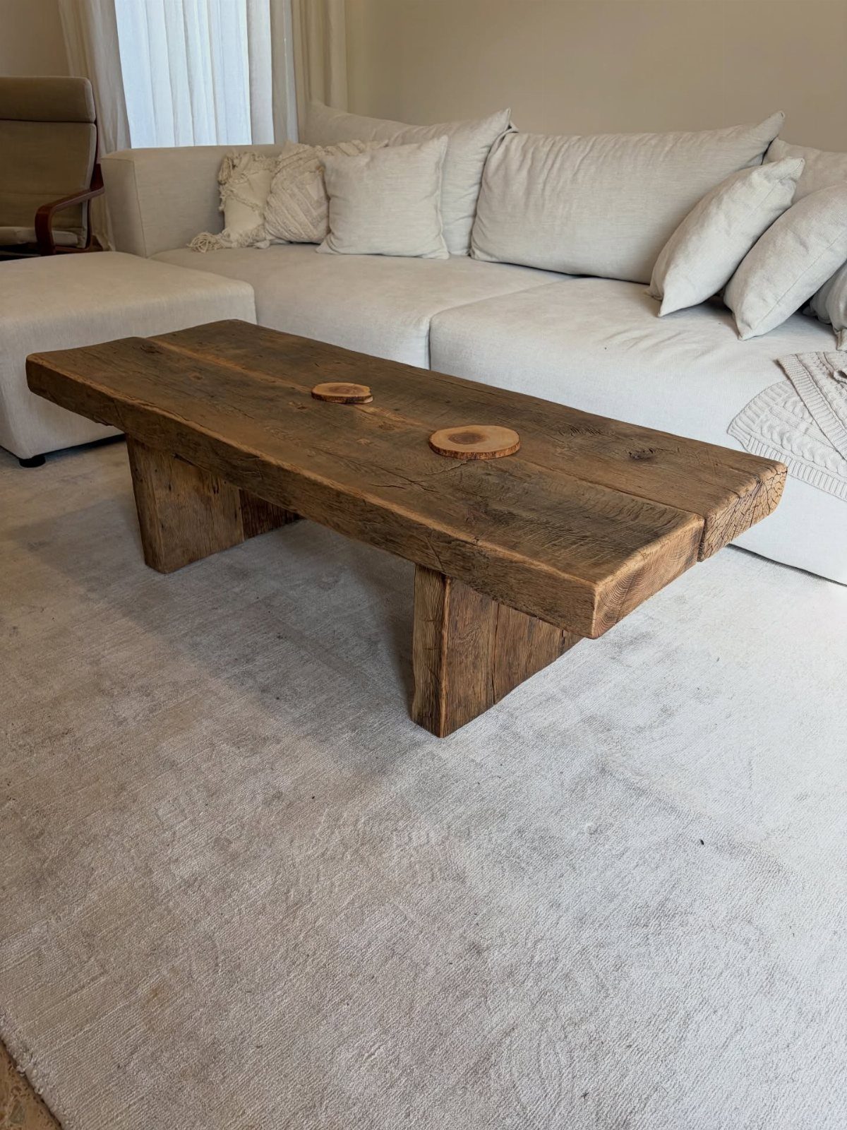 Rustic reclaimed wood coffee table on a grey rug before a white sofa.